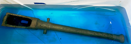 A bronze cannon in a blue liquid for conservation treatment.